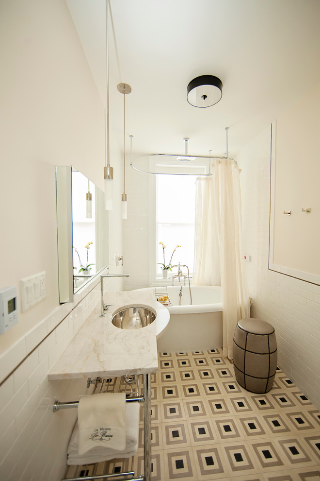 This is an example of a mid-sized contemporary 3/4 bathroom in New York with a freestanding tub, white tile, subway tile, an undermount sink, marble benchtops, a wall-mount toilet, beige walls and linoleum floors.