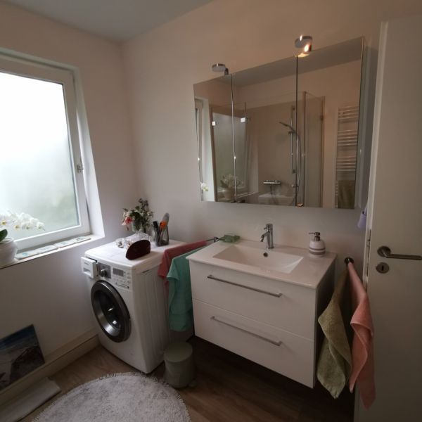 Photo of a mid-sized scandinavian 3/4 bathroom in Hamburg with flat-panel cabinets, white cabinets, a two-piece toilet, beige tile, stone tile, white walls, wood-look tile, a wall-mount sink, glass benchtops, brown floor, an open shower, a shower seat, a single vanity, a floating vanity, wallpaper and wallpaper.