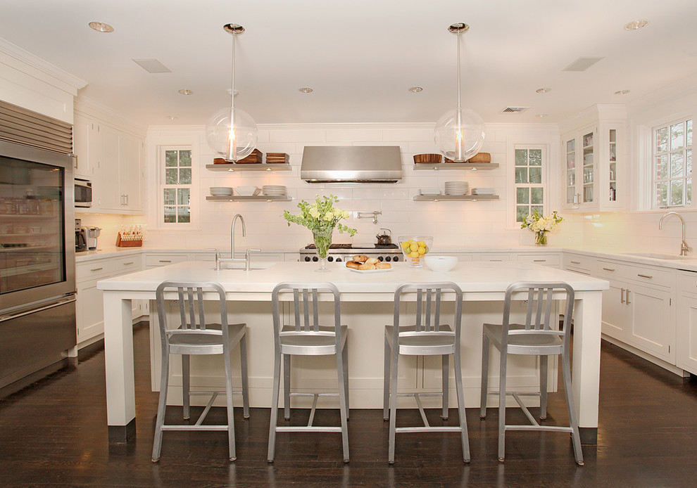 Example of a transitional u-shaped dark wood floor kitchen design with an undermount sink, shaker cabinets, white cabinets, white backsplash, stainless steel appliances and an island