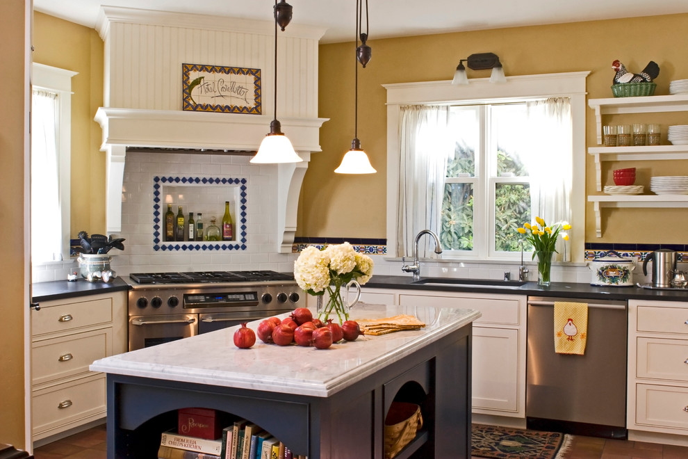 Inspiration for a mid-sized traditional l-shaped separate kitchen in Santa Barbara with an undermount sink, white cabinets, white splashback, subway tile splashback, stainless steel appliances, terra-cotta floors, with island, recessed-panel cabinets, red floor and black benchtop.