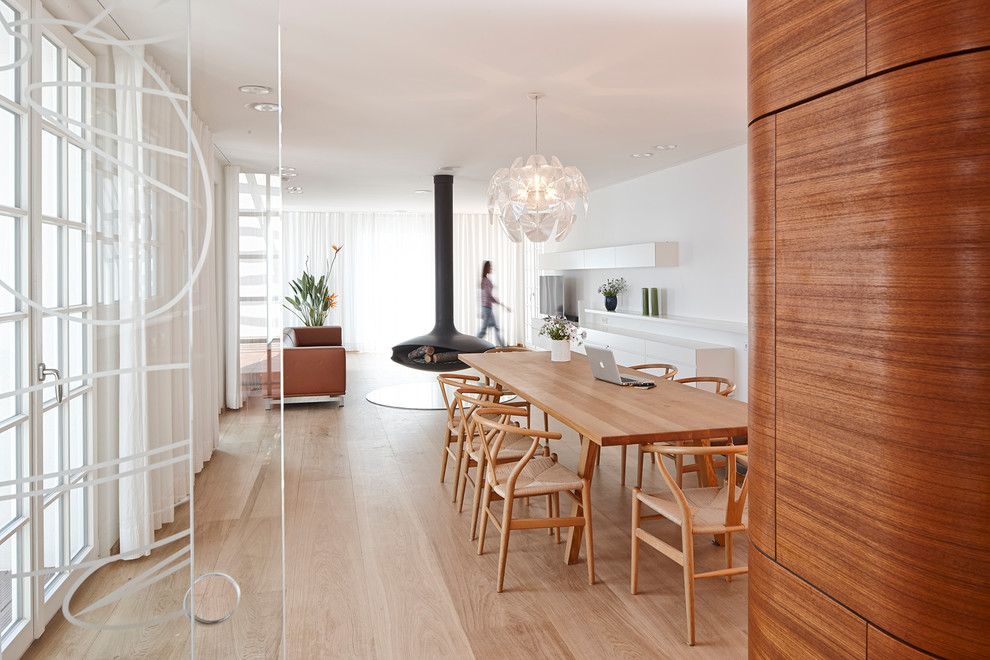 Inspiration for a mid-sized contemporary open plan dining in Stuttgart with white walls, light hardwood floors and a hanging fireplace.