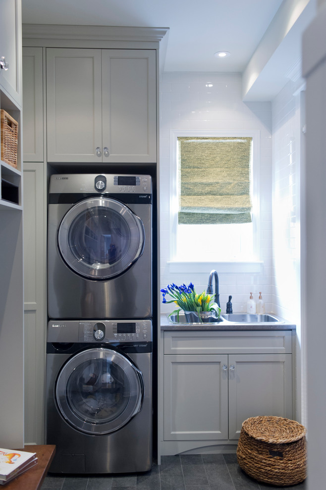 Photo of a small transitional single-wall utility room in Toronto with a drop-in sink, shaker cabinets, grey cabinets, laminate benchtops, white walls, ceramic floors and a stacked washer and dryer.