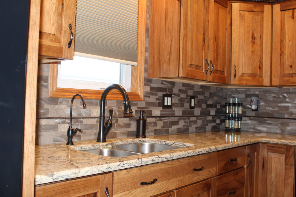 Open concept kitchen - large rustic l-shaped medium tone wood floor and brown floor open concept kitchen idea with an undermount sink, raised-panel cabinets, brown cabinets, quartzite countertops, metallic backsplash, black appliances, an island and brown countertops