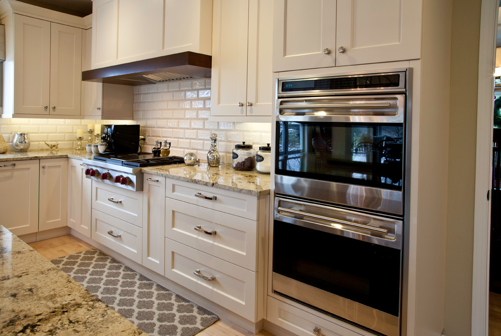 Inspiration for a large transitional l-shaped light wood floor and brown floor open concept kitchen remodel with an undermount sink, shaker cabinets, white cabinets, granite countertops, white backsplash, subway tile backsplash, paneled appliances and an island