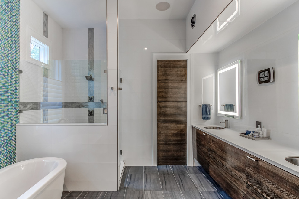 Inspiration for a large contemporary master bathroom in Wilmington with grey cabinets, a freestanding tub, white tile, porcelain tile, white walls, porcelain floors, an integrated sink, solid surface benchtops, grey floor, a hinged shower door and white benchtops.