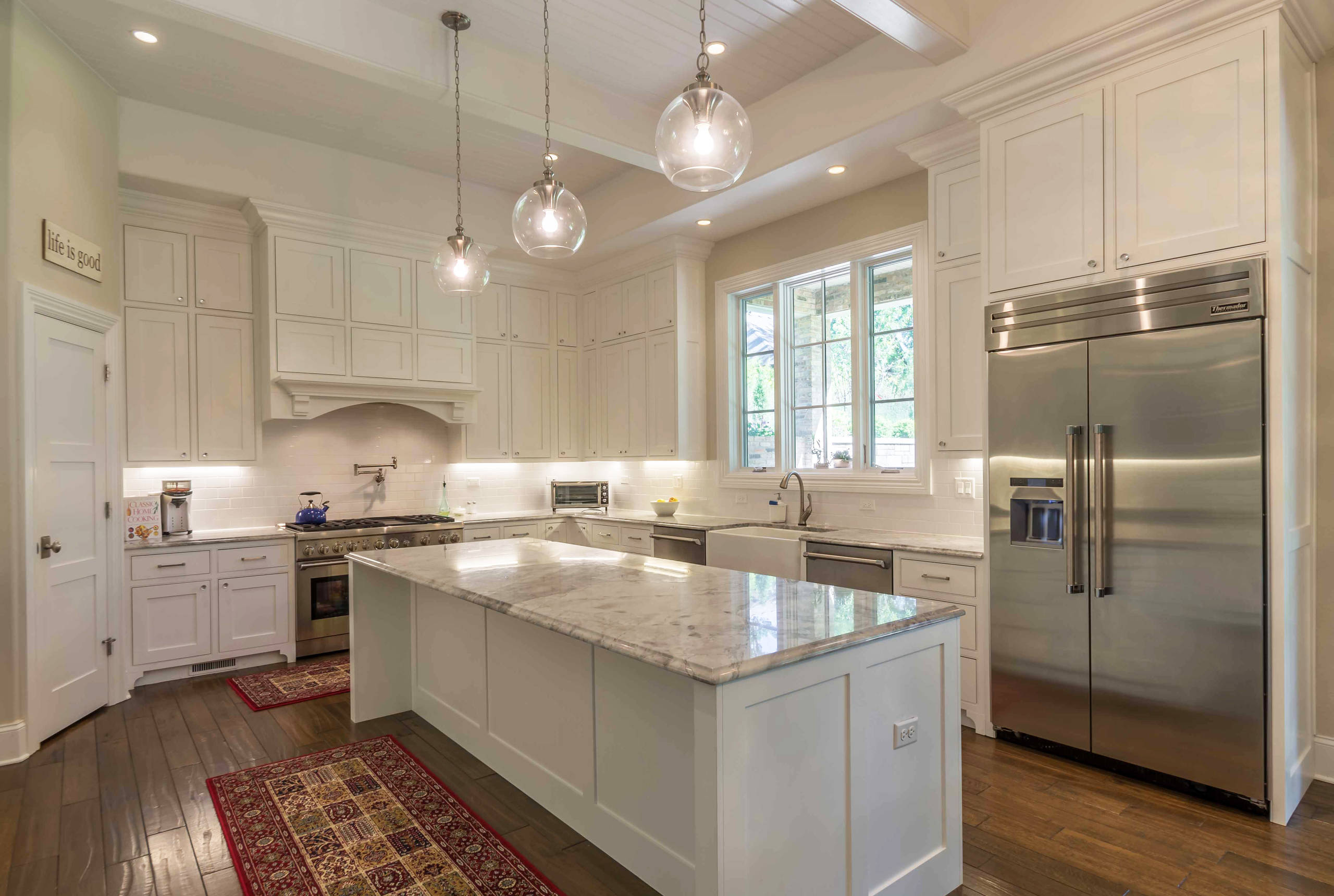 Bright white kitchen with marble island and farmhouse sink centered on large windows framing an amazing view.
