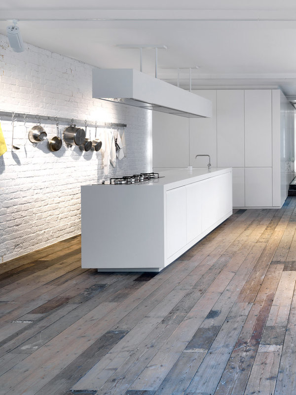 This is an example of an industrial open plan kitchen in London with an integrated sink, flat-panel cabinets, white cabinets, solid surface benchtops, white splashback, medium hardwood floors and with island.