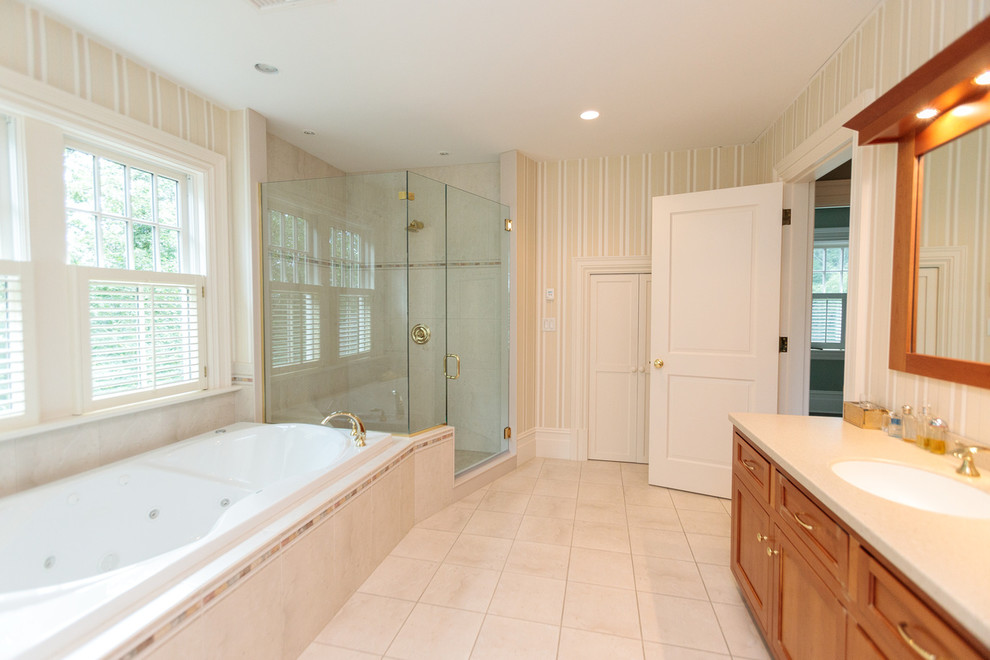 This is an example of an expansive traditional master bathroom in Boston with recessed-panel cabinets, medium wood cabinets, a drop-in tub, a corner shower, ceramic floors, a drop-in sink, solid surface benchtops, beige floor, a hinged shower door and beige benchtops.