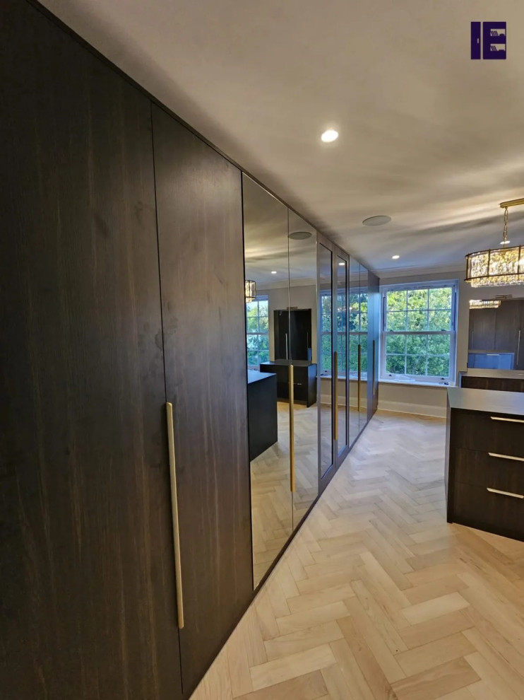 Foto di una grande cabina armadio minimalista con ante di vetro, ante in legno bruno e pavimento in compensato