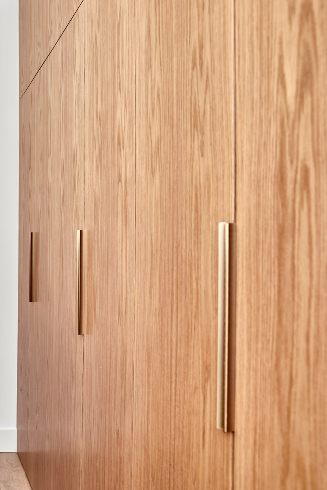 Imagen de armario vestidor actual de tamaño medio con puertas de armario de madera clara y suelo de madera clara
