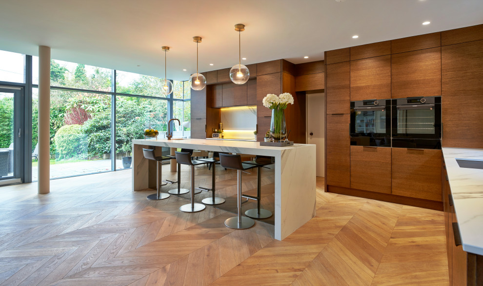 This is an example of a large contemporary l-shaped open plan kitchen in Other with flat-panel cabinets, quartzite benchtops, white splashback, ceramic splashback, black appliances, with island, white benchtop, an undermount sink, medium wood cabinets, medium hardwood floors and brown floor.