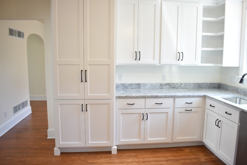Mid-sized transitional u-shaped medium tone wood floor and brown floor home design photo with an undermount sink, recessed-panel cabinets, white cabinets, marble countertops, stainless steel appliances, no island and multicolored countertops