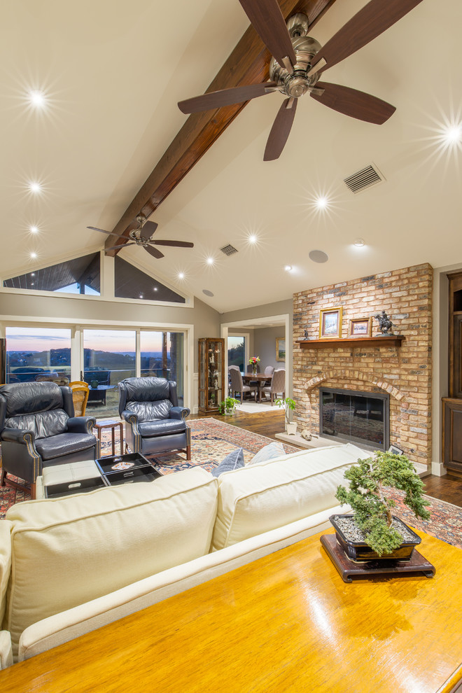 Photo of a large traditional family room in Austin with beige walls, medium hardwood floors, a standard fireplace, a brick fireplace surround and a concealed tv.