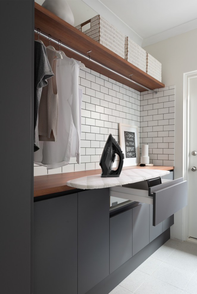 Inspiration for a mid-sized modern galley utility room in Perth with a drop-in sink, grey cabinets, wood benchtops, white splashback, ceramic splashback, ceramic floors, a side-by-side washer and dryer, beige floor and brown benchtop.