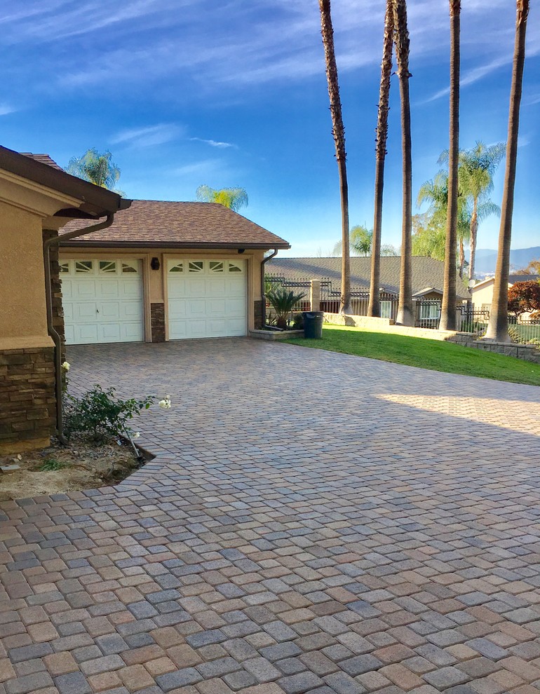 Photo of a large traditional front yard partial sun driveway in Orange County with a retaining wall and brick pavers.