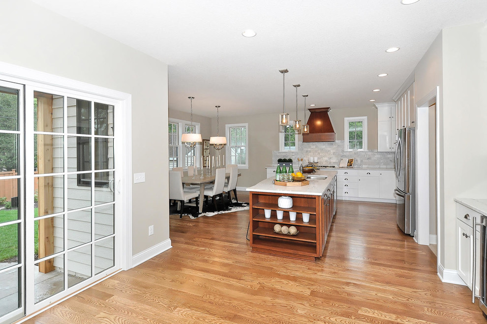 Large transitional l-shaped medium tone wood floor and brown floor eat-in kitchen photo in Minneapolis with a double-bowl sink, shaker cabinets, white cabinets, quartz countertops, gray backsplash, marble backsplash, stainless steel appliances, an island and white countertops