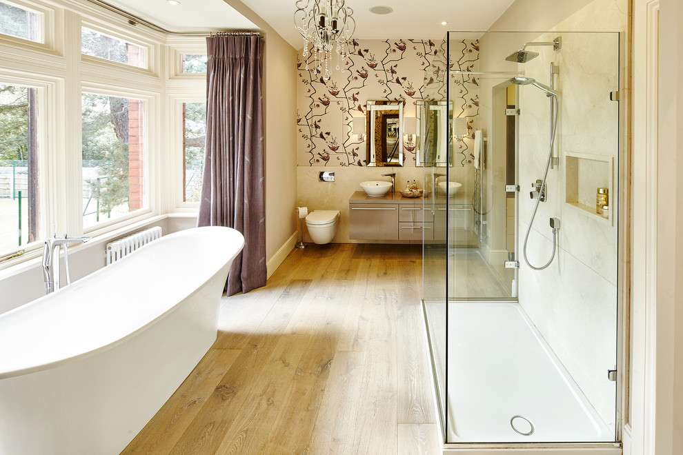 This is an example of a large transitional master bathroom in Other with a vessel sink, flat-panel cabinets, light wood cabinets, a freestanding tub, a wall-mount toilet, beige tile, multi-coloured walls and light hardwood floors.