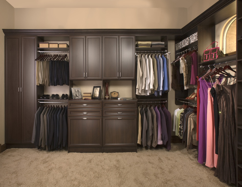 This is an example of a traditional gender-neutral walk-in wardrobe in Orange County with recessed-panel cabinets, dark wood cabinets and carpet.