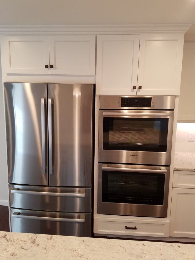 Mid-sized transitional l-shaped dark wood floor and brown floor eat-in kitchen photo with a farmhouse sink, shaker cabinets, white cabinets, granite countertops, white backsplash, subway tile backsplash, stainless steel appliances and an island