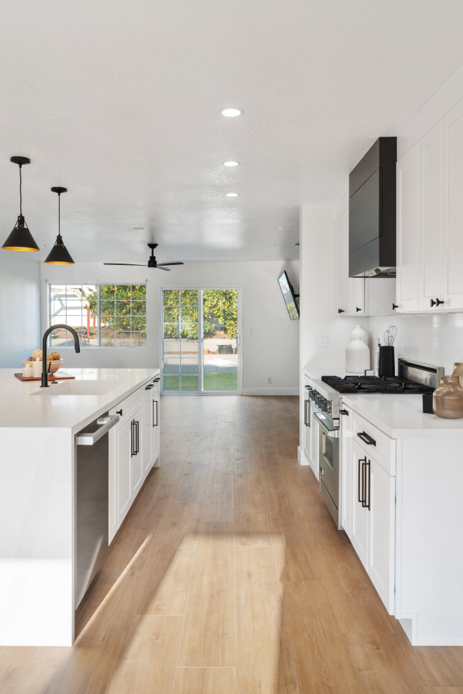 Inspiration for a mid-sized transitional vinyl floor and brown floor open concept kitchen remodel in Orange County with an undermount sink, shaker cabinets, white cabinets, quartz countertops, white backsplash, quartz backsplash, stainless steel appliances, an island and white countertops