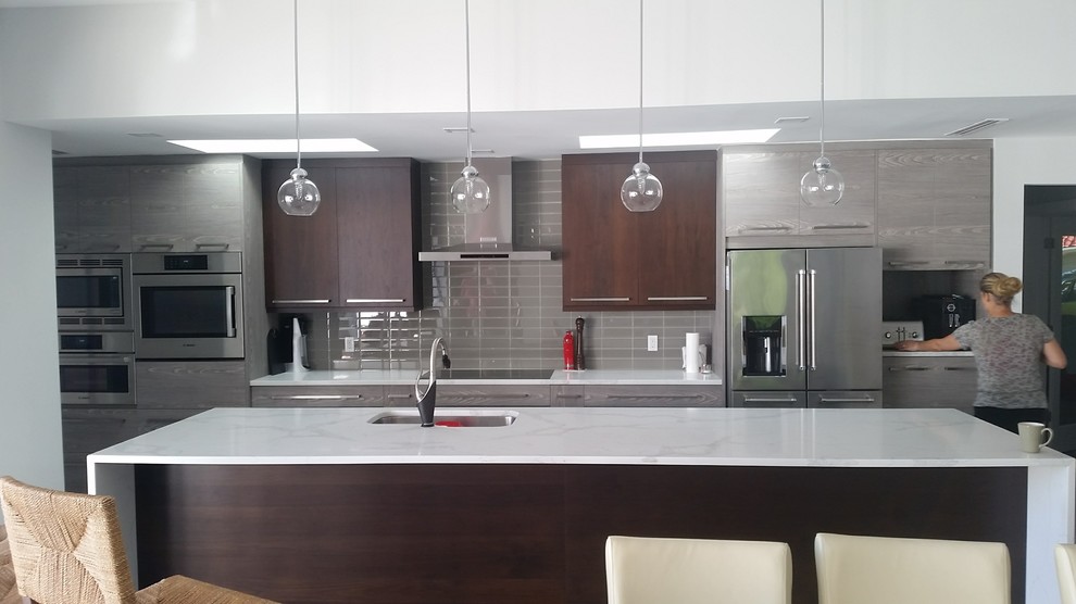 Photo of a mid-sized modern galley open plan kitchen in Tampa with a single-bowl sink, flat-panel cabinets, medium wood cabinets, quartz benchtops, beige splashback, glass tile splashback, stainless steel appliances, porcelain floors, with island and grey floor.
