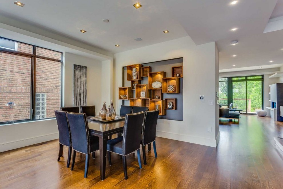 This is an example of a large modern dining room in Toronto with white walls, medium hardwood floors and a wood fireplace surround.