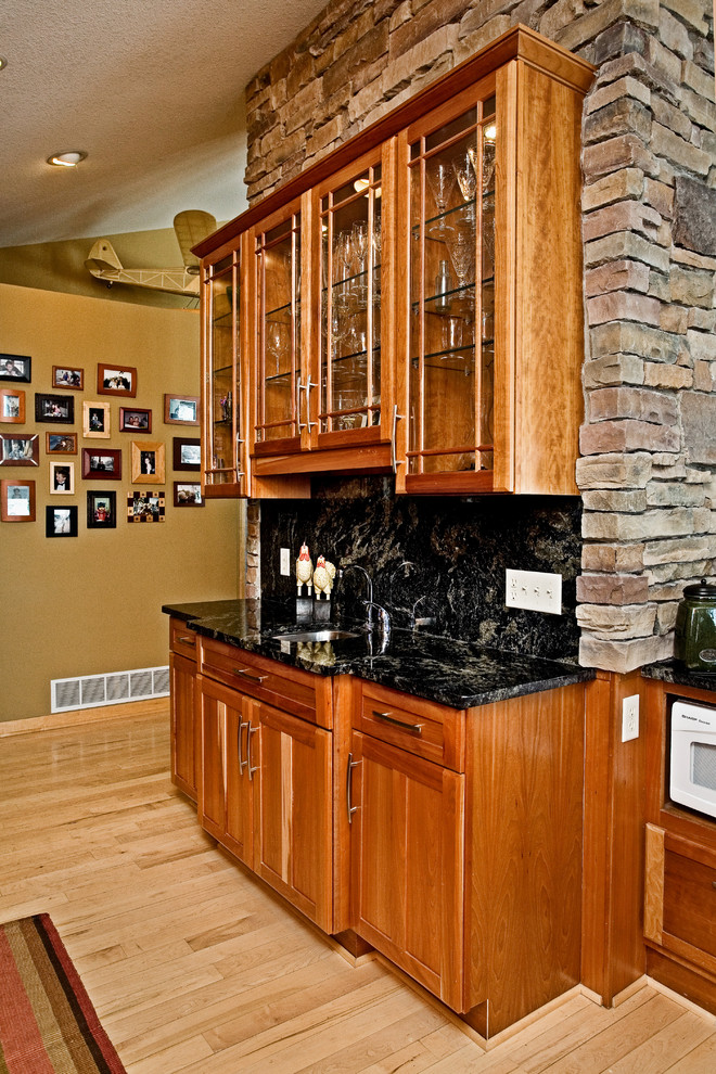 Photo of an arts and crafts kitchen in Minneapolis with an undermount sink, glass-front cabinets, medium wood cabinets, granite benchtops, black splashback, stone slab splashback, white appliances and light hardwood floors.