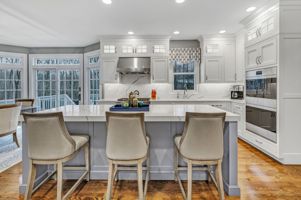 Klassische Küche mit weißen Schränken, Quarzwerkstein-Arbeitsplatte, Rückwand aus Quarzwerkstein, Elektrogeräten mit Frontblende, braunem Holzboden und Kücheninsel in New York