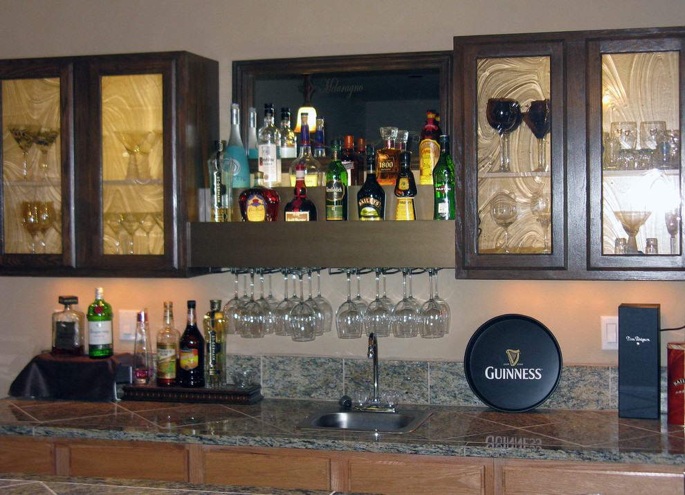 This is an example of a large mediterranean galley seated home bar in Denver with glass-front cabinets, dark wood cabinets, granite benchtops and porcelain floors.