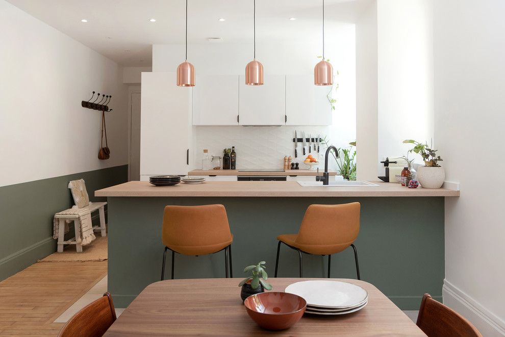 This is an example of a scandinavian galley eat-in kitchen in Lyon with a drop-in sink, flat-panel cabinets, white cabinets, white splashback, medium hardwood floors, a peninsula, brown floor and beige benchtop.