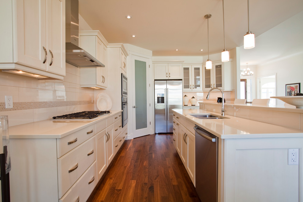 Inspiration for a transitional l-shaped dark wood floor open concept kitchen remodel in Edmonton with a double-bowl sink, shaker cabinets, white cabinets, white backsplash, ceramic backsplash, stainless steel appliances and an island