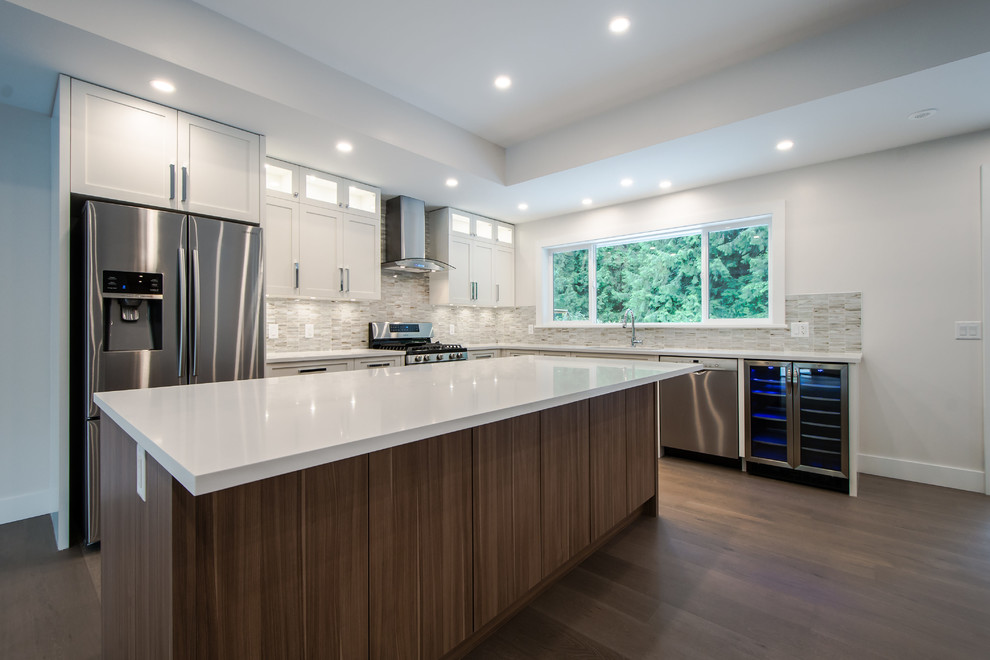 Photo of a large contemporary l-shaped open plan kitchen in Vancouver with an undermount sink, shaker cabinets, white cabinets, stainless steel appliances, with island, medium hardwood floors, grey splashback, matchstick tile splashback and quartz benchtops.