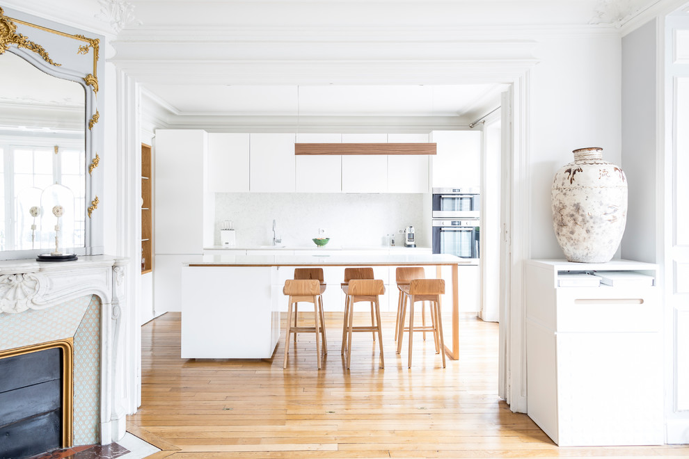 This is an example of a large contemporary galley open plan kitchen in Paris with flat-panel cabinets, white cabinets, white splashback, stainless steel appliances, light hardwood floors, with island, beige floor, a single-bowl sink and white benchtop.