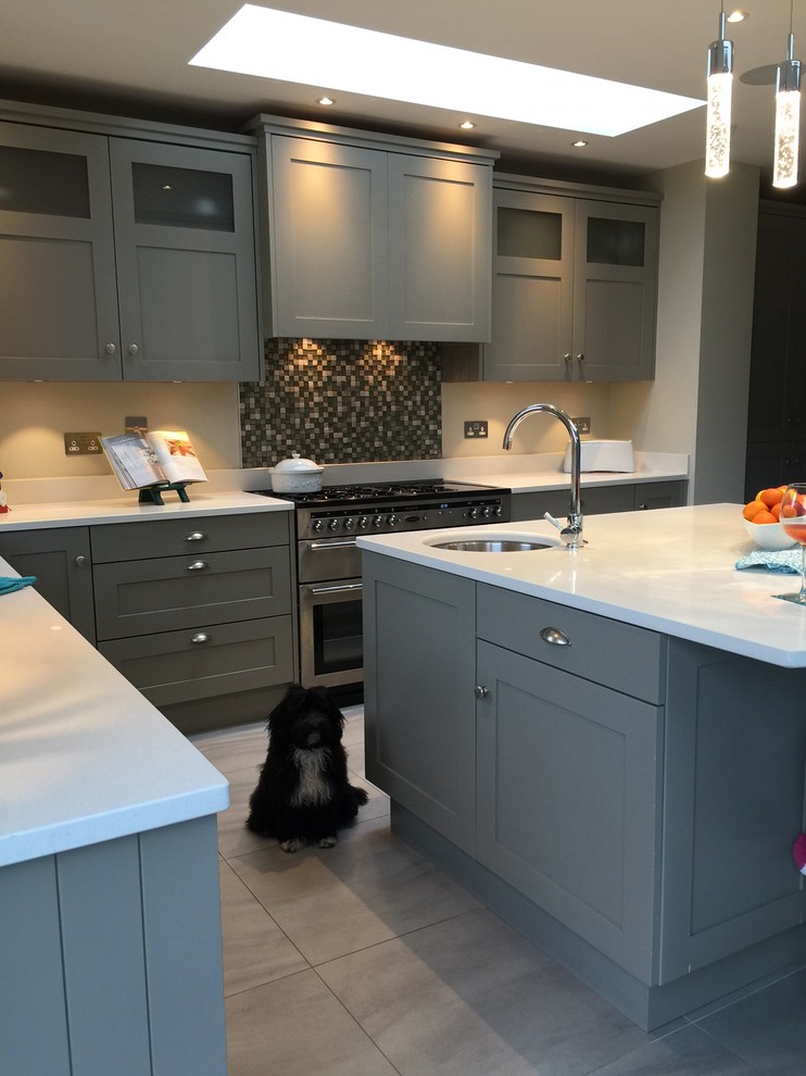 Mid-sized transitional l-shaped eat-in kitchen in Dublin with an undermount sink, shaker cabinets, grey cabinets, quartz benchtops, multi-coloured splashback, mosaic tile splashback, stainless steel appliances, porcelain floors, with island and grey floor.