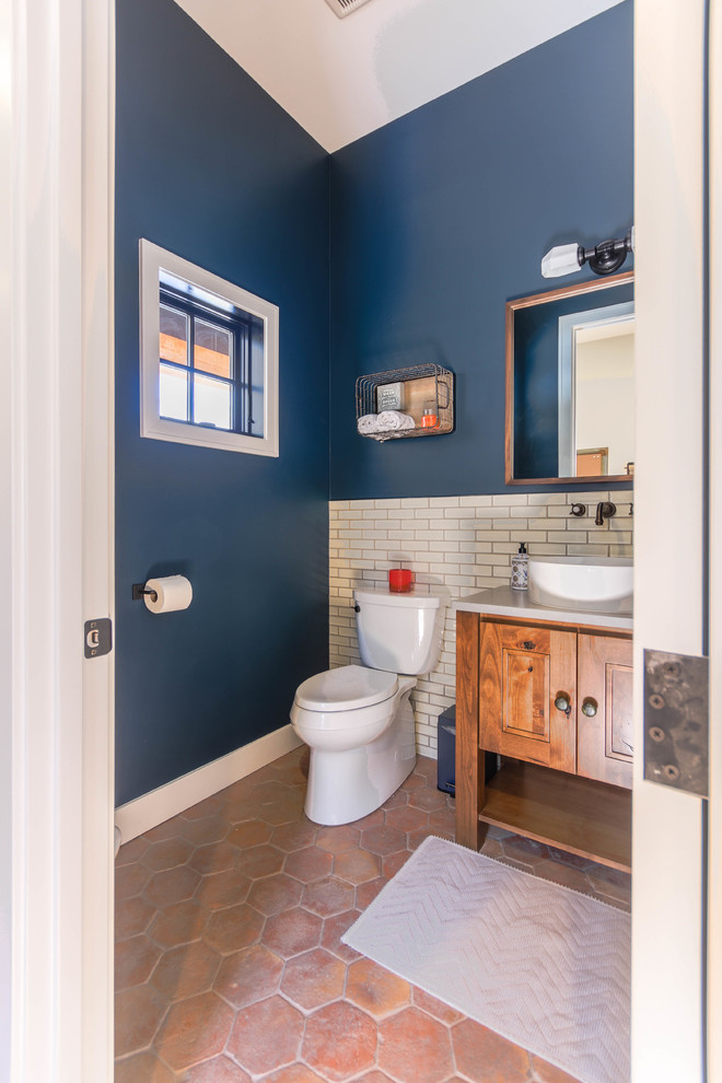 This is an example of a mid-sized country 3/4 bathroom in Detroit with raised-panel cabinets, distressed cabinets, a one-piece toilet, white tile, subway tile, blue walls, porcelain floors, a vessel sink, engineered quartz benchtops, orange floor and white benchtops.