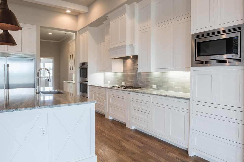 Example of a large transitional u-shaped medium tone wood floor and brown floor eat-in kitchen design in Dallas with a drop-in sink, recessed-panel cabinets, white cabinets, granite countertops, beige backsplash, ceramic backsplash, stainless steel appliances, an island and multicolored countertops
