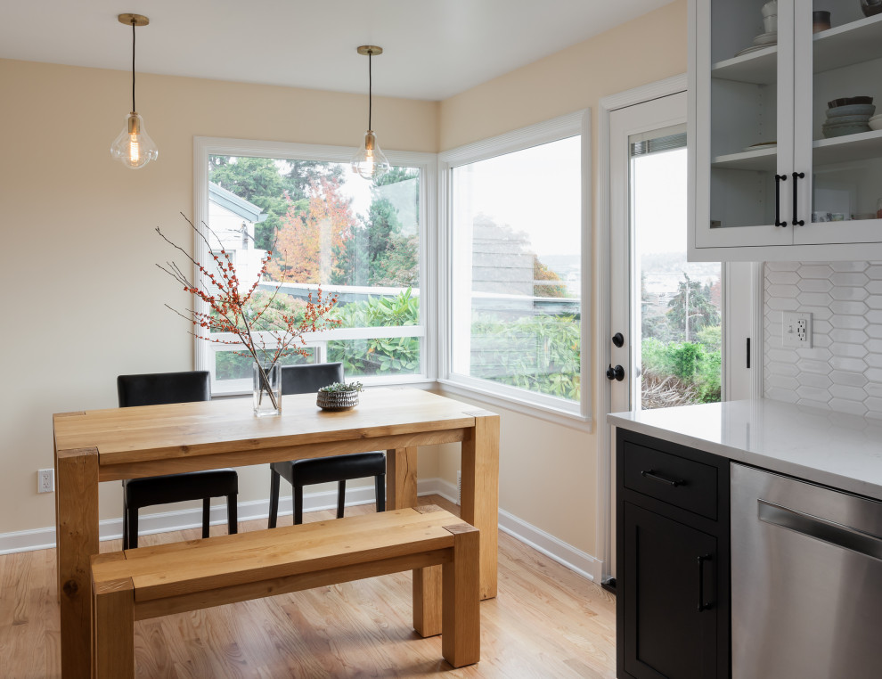 Small traditional u-shaped eat-in kitchen in Seattle with a single-bowl sink, shaker cabinets, black cabinets, quartz benchtops, white splashback, stainless steel appliances, light hardwood floors, no island and white benchtop.