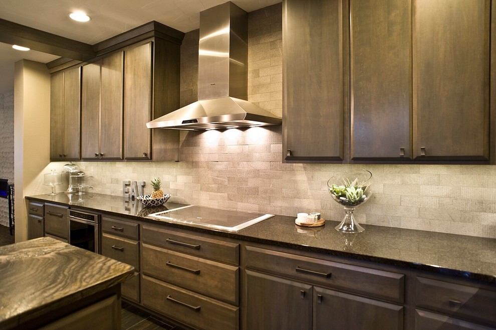 Example of a transitional dark wood floor kitchen design with stainless steel appliances, brown cabinets, granite countertops, gray backsplash, stone tile backsplash and an island