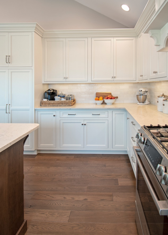 Eat-in kitchen - transitional medium tone wood floor, brown floor and vaulted ceiling eat-in kitchen idea with shaker cabinets, white cabinets, quartz countertops, white backsplash, ceramic backsplash, stainless steel appliances, an island and white countertops
