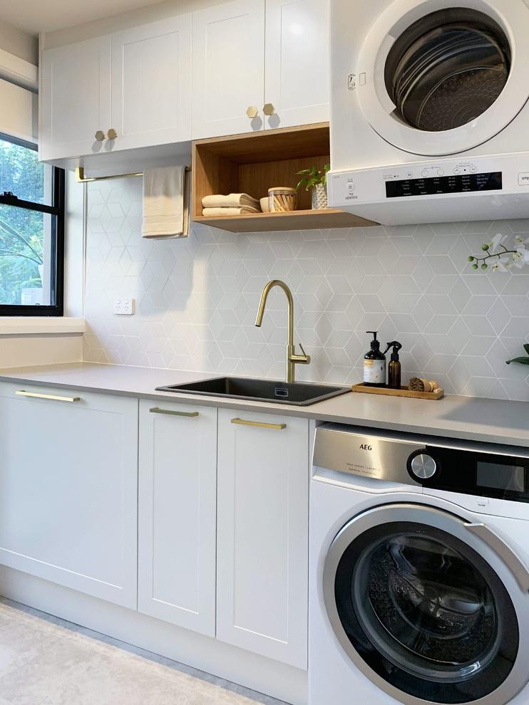 Photo of a small contemporary single-wall dedicated laundry room in Sydney with a drop-in sink, shaker cabinets, white cabinets, quartz benchtops, grey walls, ceramic floors, a stacked washer and dryer, grey floor and grey benchtop.