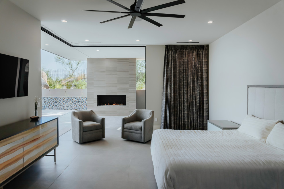 Photo of a large contemporary master bedroom in Phoenix with white walls, porcelain flooring, a standard fireplace, a tiled fireplace surround and grey floors.