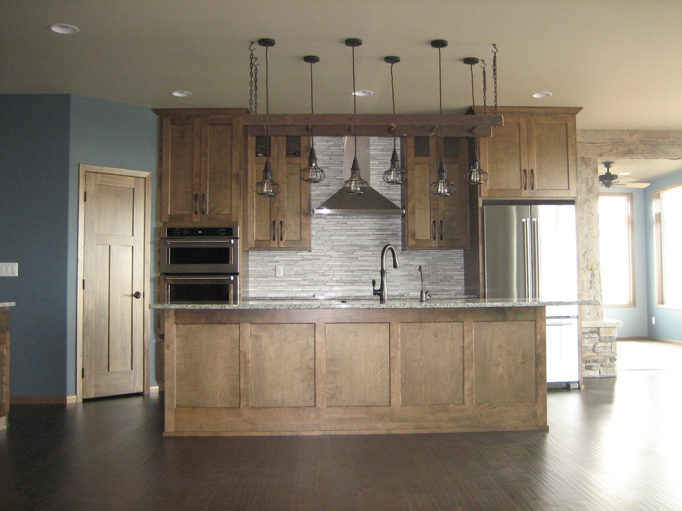 Open concept kitchen - mid-sized rustic l-shaped dark wood floor open concept kitchen idea with an undermount sink, recessed-panel cabinets, medium tone wood cabinets, granite countertops, gray backsplash, glass tile backsplash, stainless steel appliances and an island