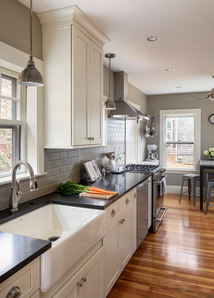 Inspiration for a mid-sized transitional galley light wood floor kitchen pantry remodel in Boston with a farmhouse sink, shaker cabinets, white cabinets, granite countertops, gray backsplash, subway tile backsplash, stainless steel appliances, no island and black countertops