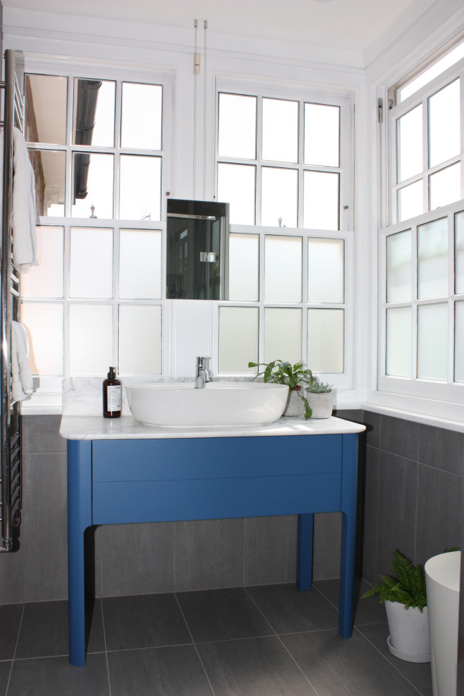 Skandinavisk inredning av ett litet vit vitt badrum med dusch, med släta luckor, blå skåp, en öppen dusch, en vägghängd toalettstol, grå kakel, skifferkakel, grå väggar, skiffergolv, ett konsol handfat, marmorbänkskiva, grått golv och dusch med gångjärnsdörr