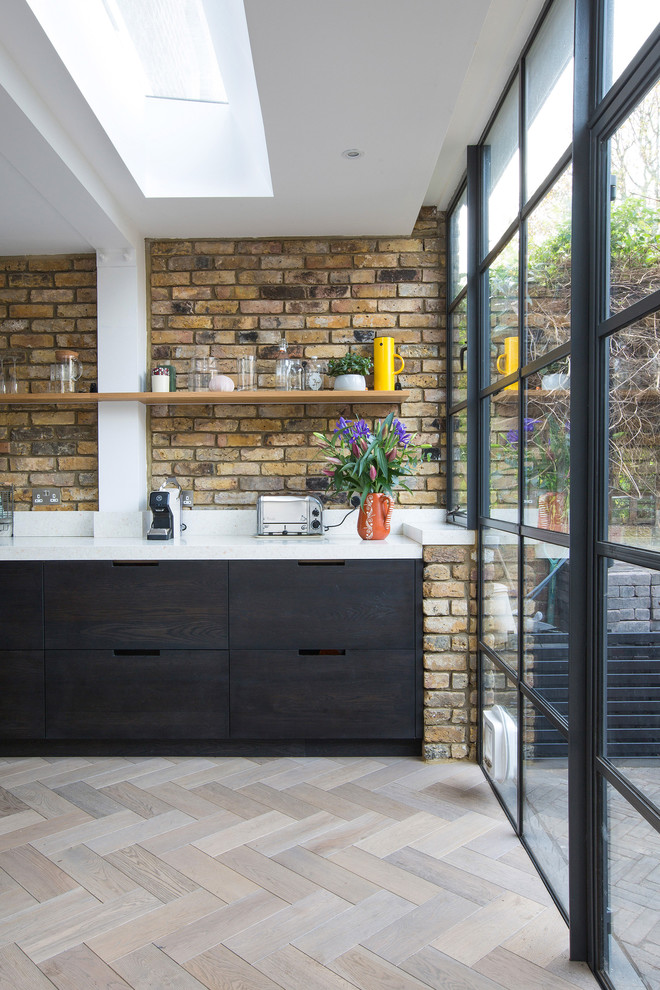 This is an example of a large contemporary single-wall open plan kitchen in London with flat-panel cabinets, black cabinets, solid surface benchtops, white splashback, medium hardwood floors, brown floor and an integrated sink.