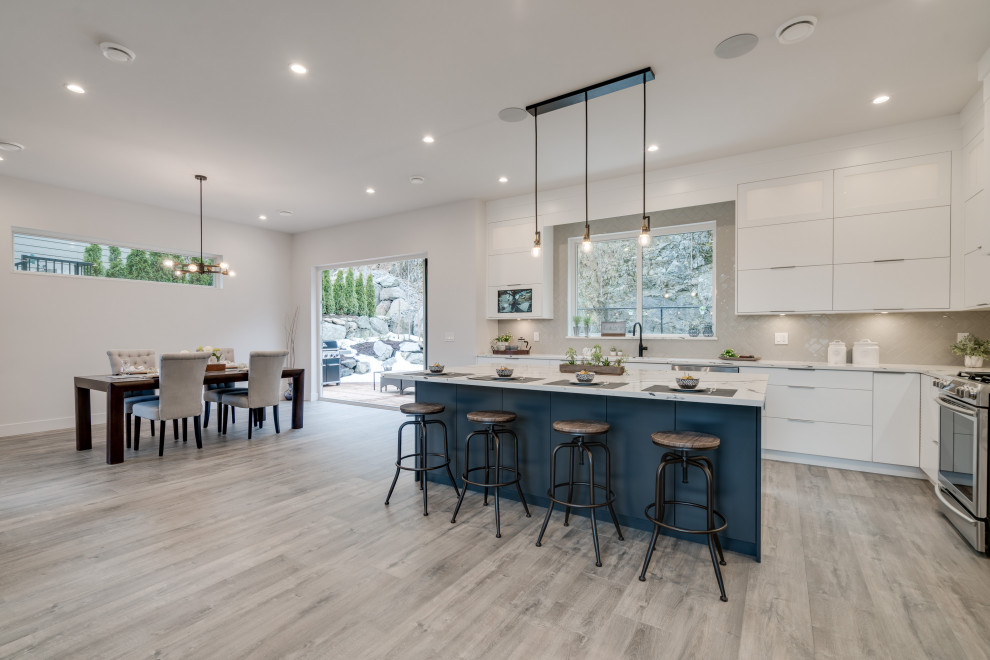 This is an example of a mid-sized contemporary l-shaped eat-in kitchen in Vancouver with a single-bowl sink, flat-panel cabinets, white cabinets, quartzite benchtops, beige splashback, subway tile splashback, stainless steel appliances, laminate floors, with island, grey floor and white benchtop.
