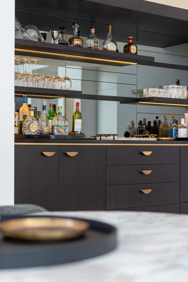 This is an example of a large contemporary single-wall wet bar in Sydney with an integrated sink, flat-panel cabinets, black cabinets, solid surface benchtops, mirror splashback, light hardwood floors and black benchtop.