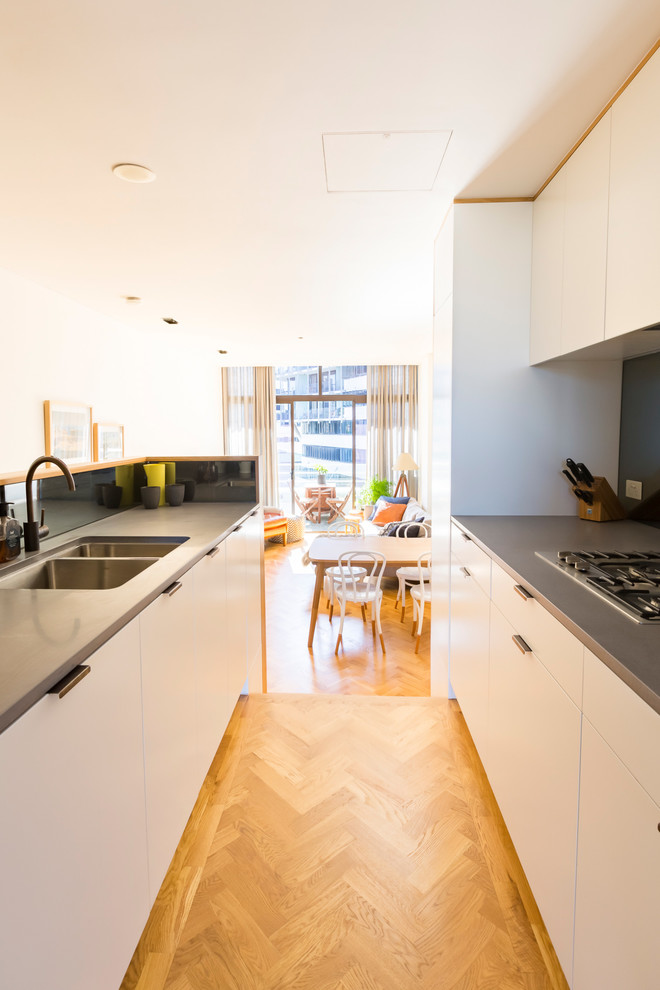Small contemporary galley separate kitchen in Sydney with an undermount sink, flat-panel cabinets, white cabinets, concrete benchtops, grey splashback, glass sheet splashback, stainless steel appliances, light hardwood floors, no island and yellow floor.