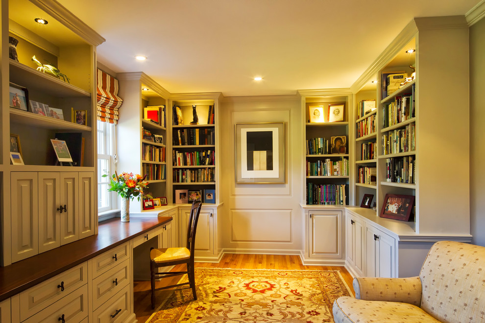 Photo of a large traditional home office in New York with a built-in desk, white walls and medium hardwood floors.