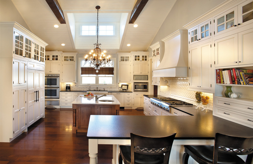 Design ideas for a large traditional u-shaped kitchen in Chicago with a farmhouse sink, recessed-panel cabinets, white cabinets, white splashback, stainless steel appliances, dark hardwood floors, brown floor, subway tile splashback and with island.